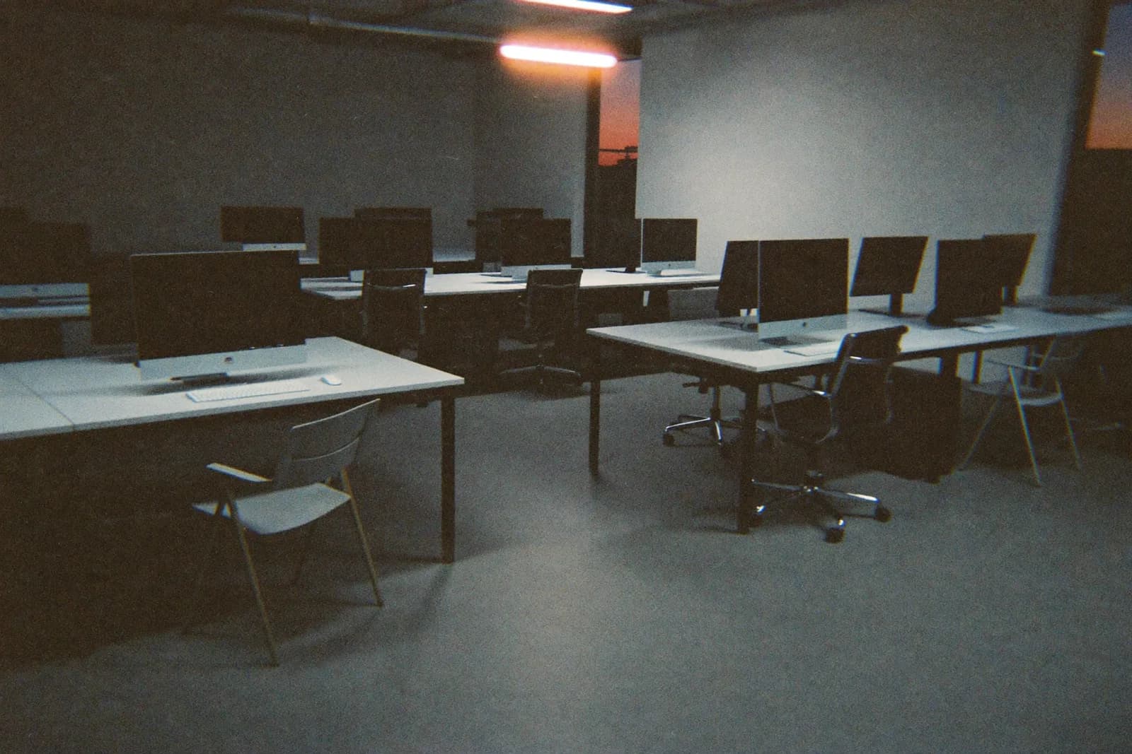 An empty startup office at dusk, rows of vacant desks with one overhead light left on.